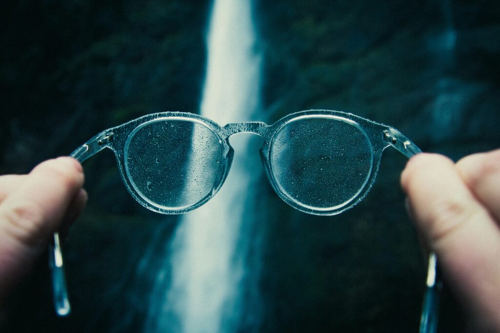 A pair of glasses in the foreground, with a waterfall visible through them in the background.